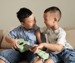 Two siblings play a ukulele together.