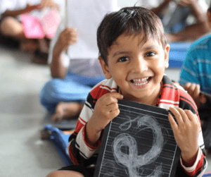 A child holds a small chalkboard with the number 2 on it