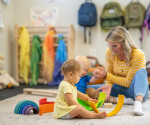 An early intervention therapist helps two babies play with a rainbow toy.