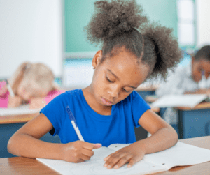 Young girl with pigtails in blue shirt writes on paper with pencil